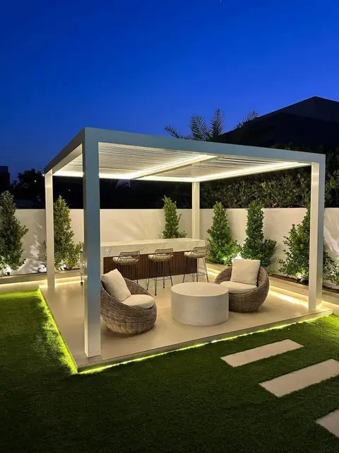 Pergola lounge illuminated at night with turf and water feature